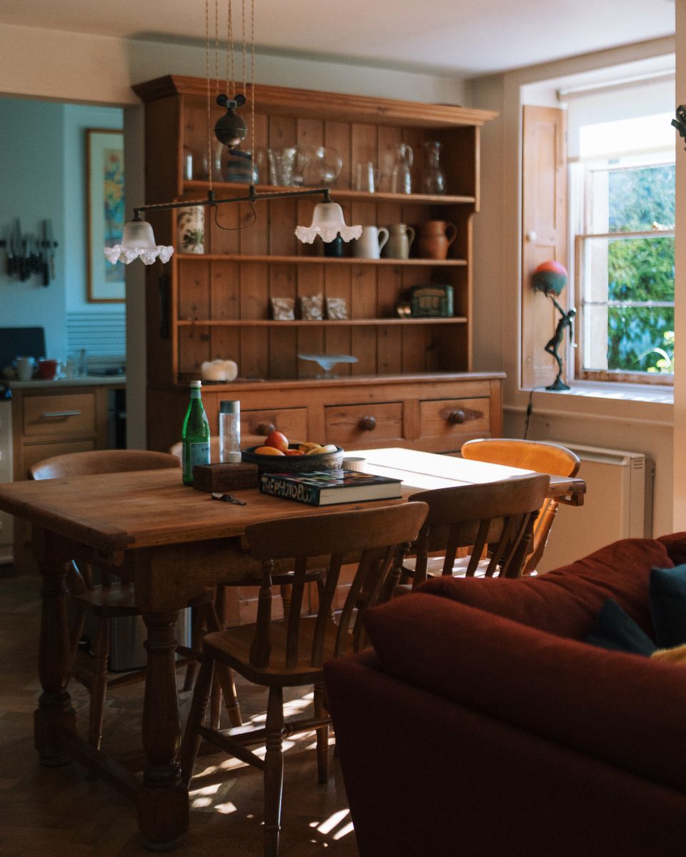 A sunny, lived-in dining room and kitchen with a wooden table.